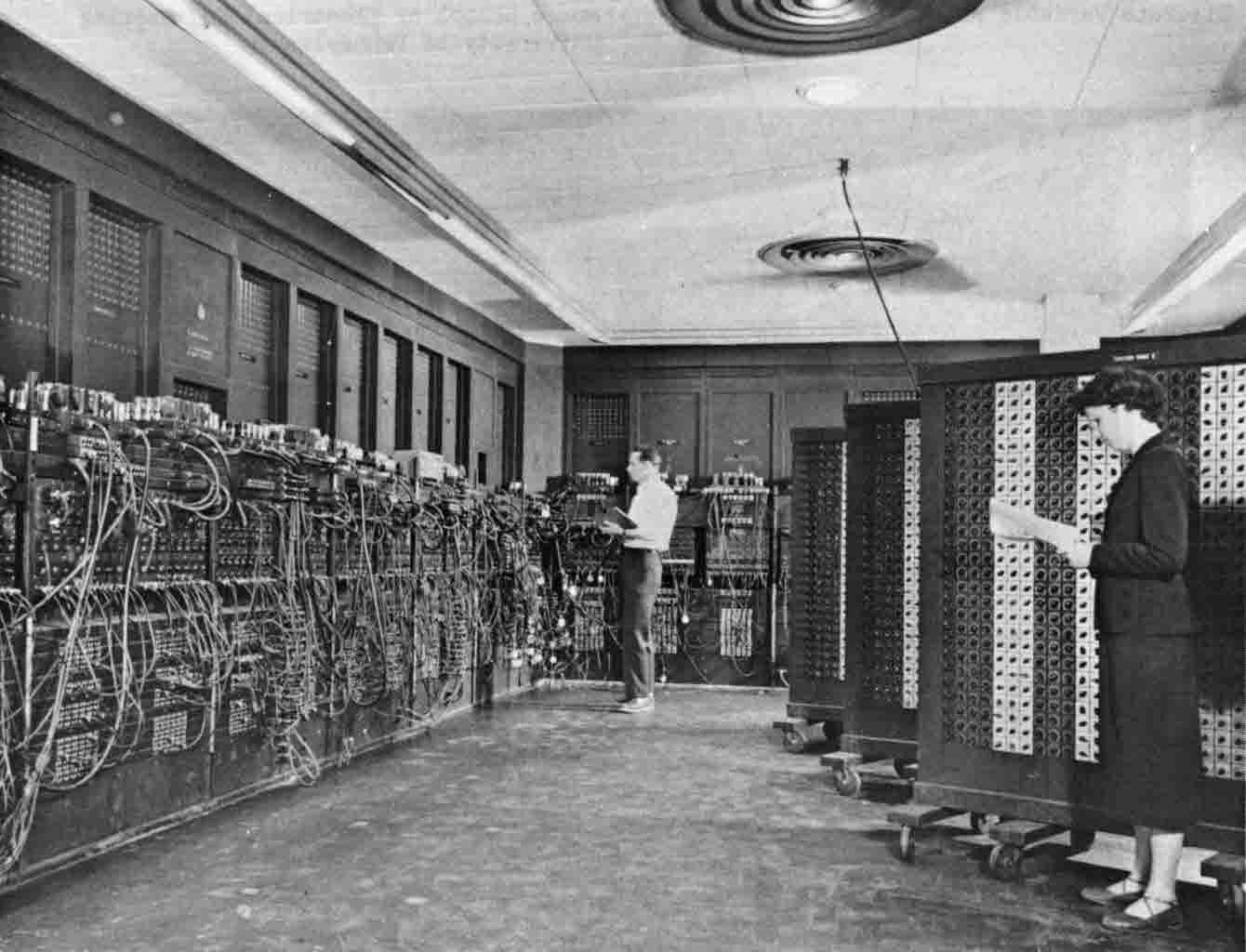 Historical ENIAC computer from the 1940s with extensive wiring, large panels, and people operating the machine in a full-sized room