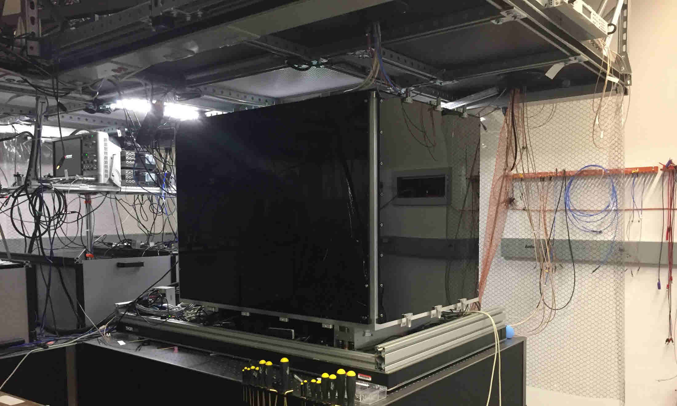 Modern ion trap quantum computer setup with black shielding box on an optical table, surrounded by cables and electronics for laser control